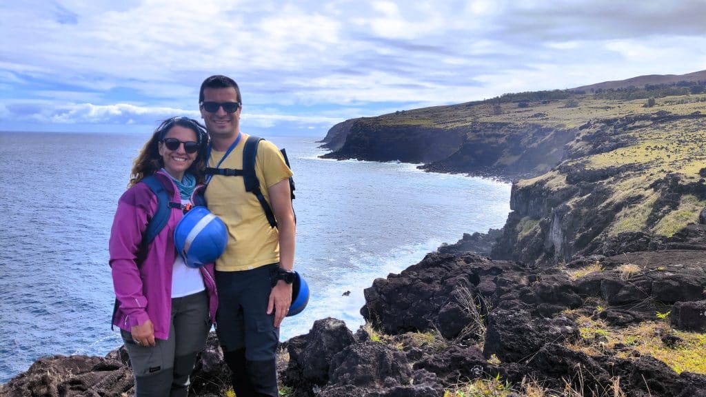Domi y Montse tras un tour por las cuevas de Rapa Nui, con cascos de seguridad y un acantilado al fondo