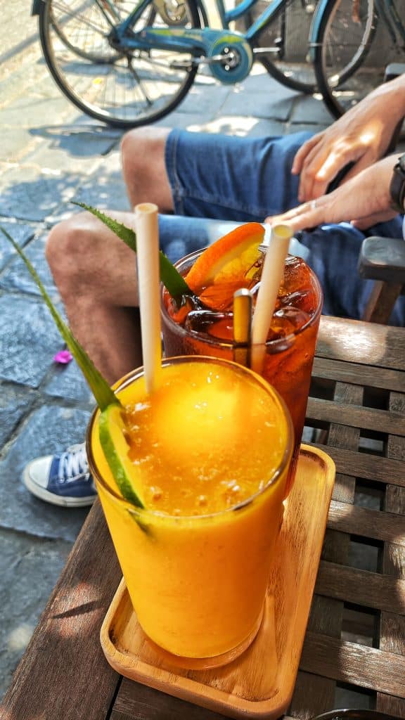 Primer plano de nuestros vasos con bebidas refrescantes mientras estamos sentados en una calle de Hoi An, con el ambiente característico de la ciudad al fondo