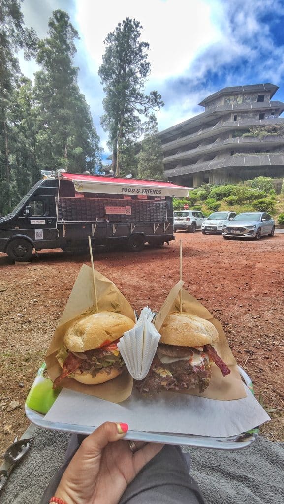 Dos hamburguesas en una bandeja en primer plano con el Food & Friends – Food Truck del Miradouro da Vista do Rei al fondo, en Sete Cidades