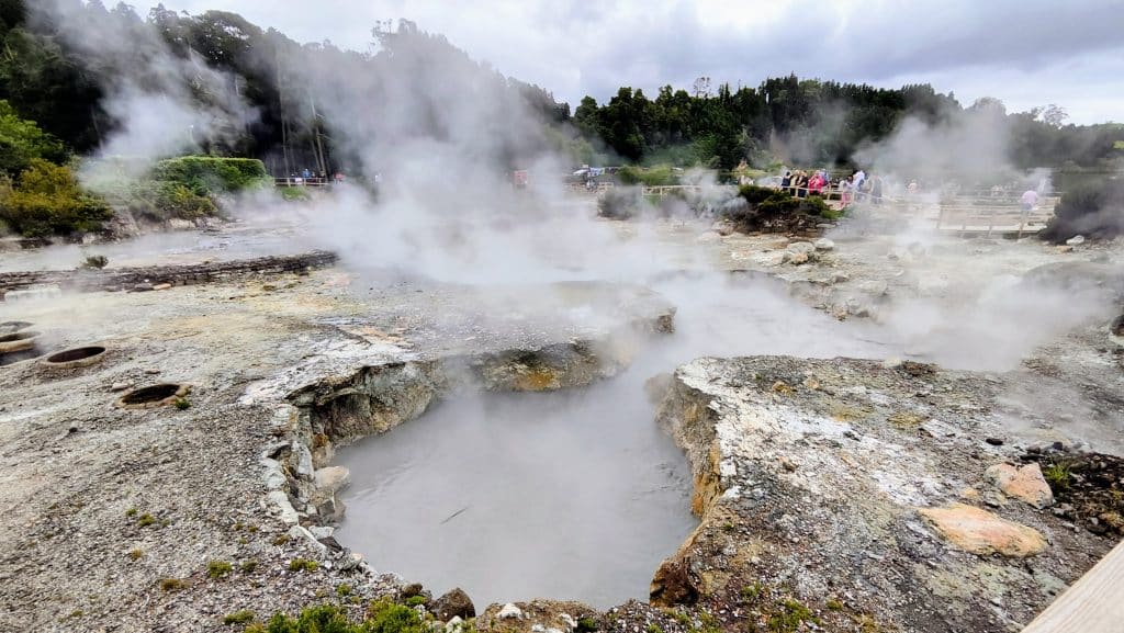 Pasarelas de madera sobre las fumarolas de Furnas, rodeadas de pozas de agua caliente y vapor que asciende del suelo, mostrando la actividad geotérmica del lugar