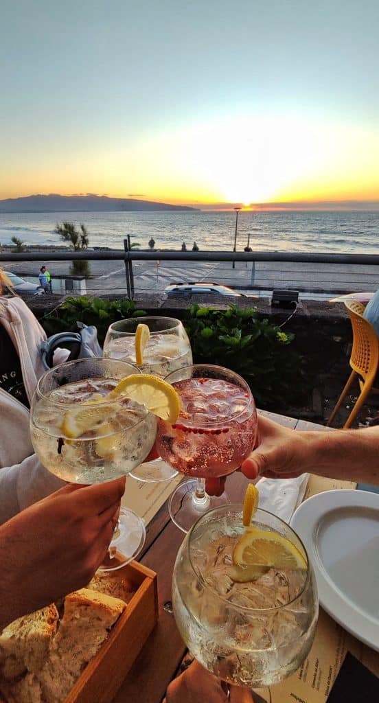 4 copas de gin tonic brindando con una puesta de sol de fondo en ribeira grande, sao miguel, azores